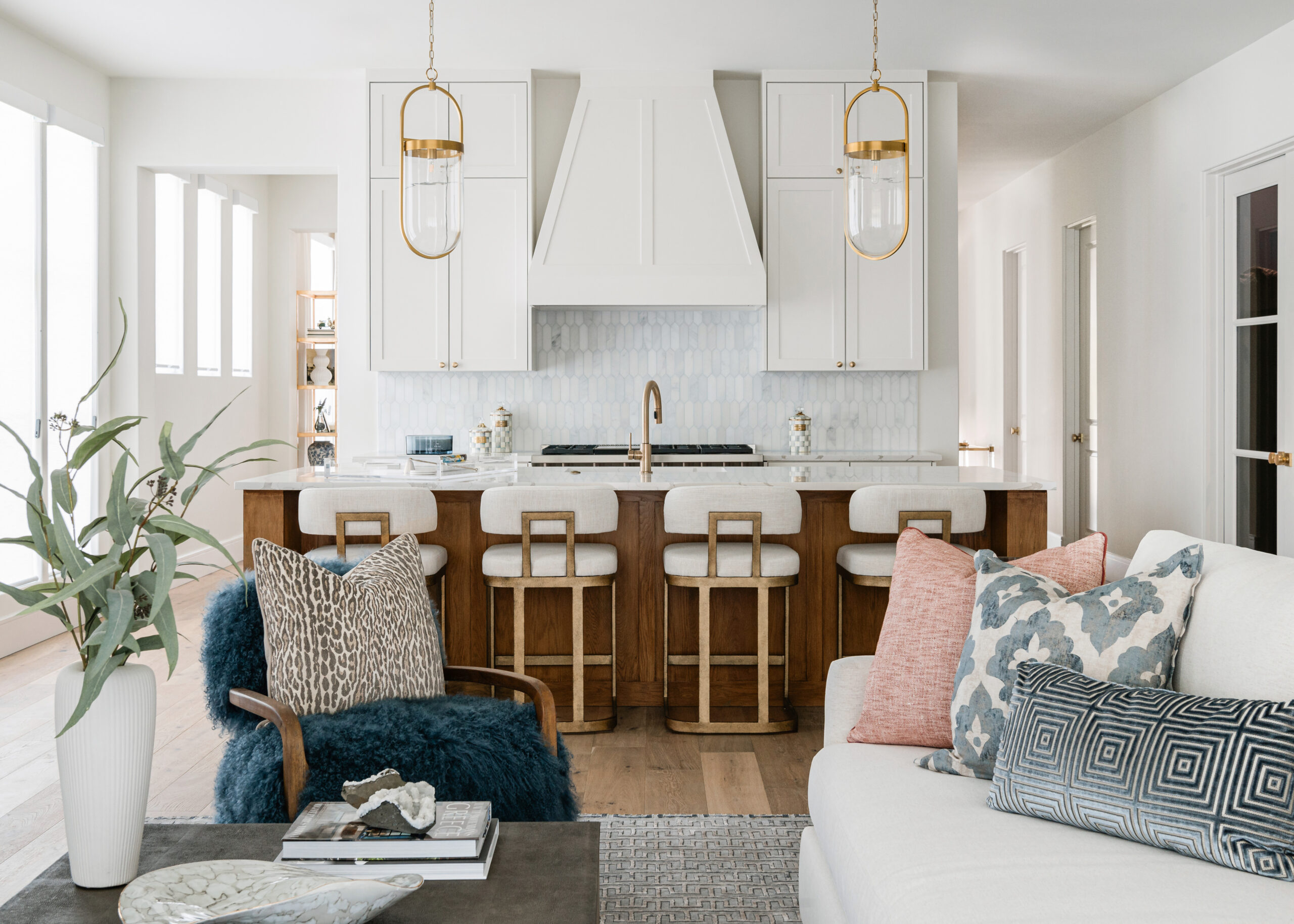 Open concept living room and kitchen: A modern, airy Texas interior design living room with cozy, plush seating, a chic coffee table, and a view of the open-concept kitchen featuring white cabinetry and warm wood elements.