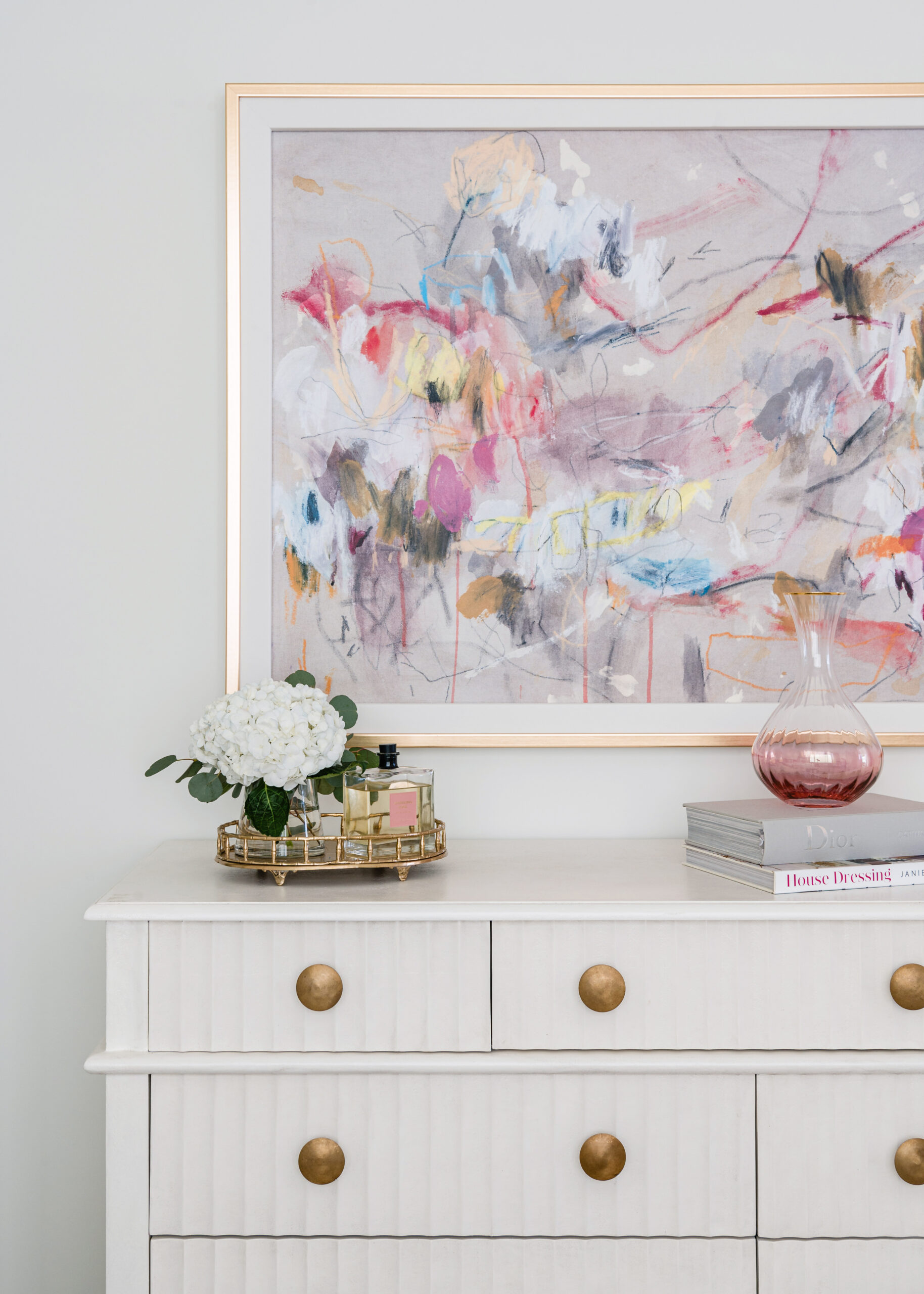 Dresser with abstract art: A sophisticated dresser topped with a floral arrangement and decorative objects, set beneath a vibrant abstract painting in a modern Texas interior design bedroom.