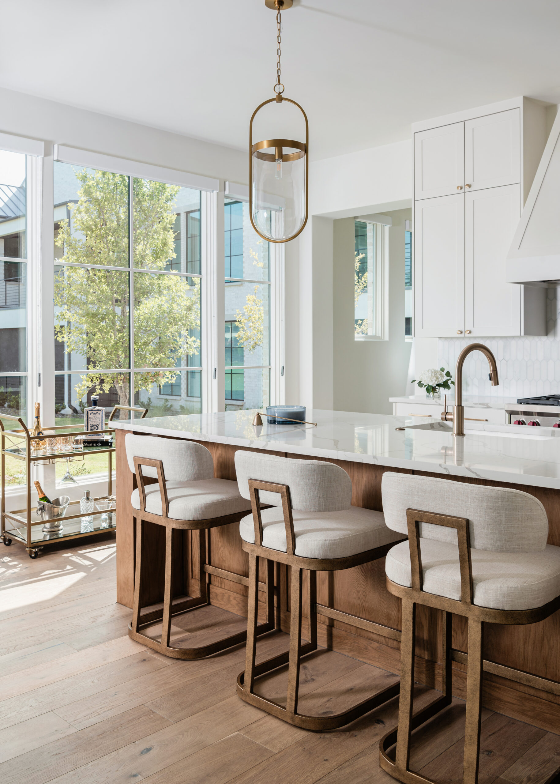 Modern Texas interior design kitchen with a large island featuring natural wood tones, cushioned barstools, and a sleek pendant light, framed by expansive windows that flood the space with natural light