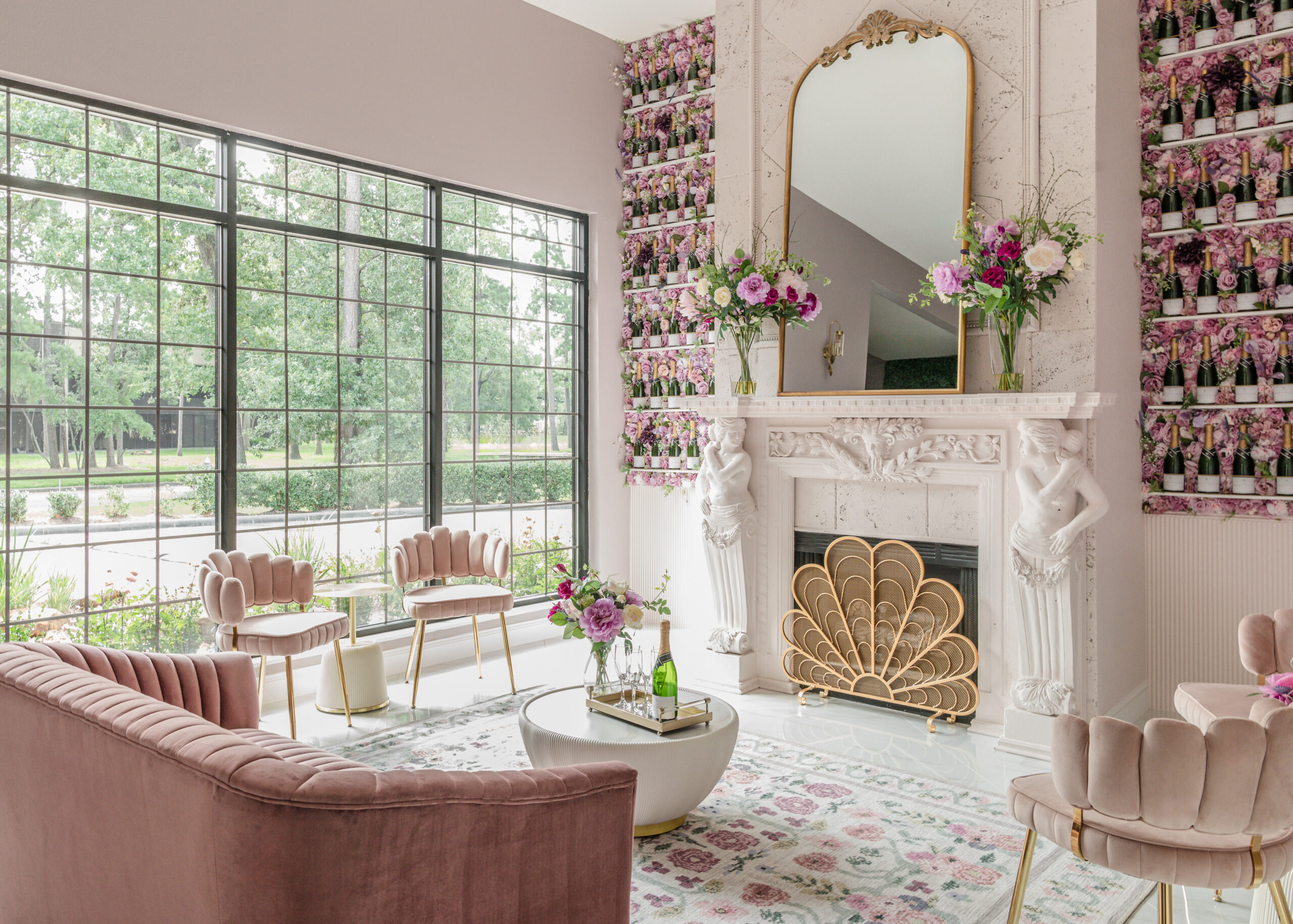 A cozy seating area in a bridal boutique with pink velvet chairs, a marble fireplace with decorative molding, and soft lighting.