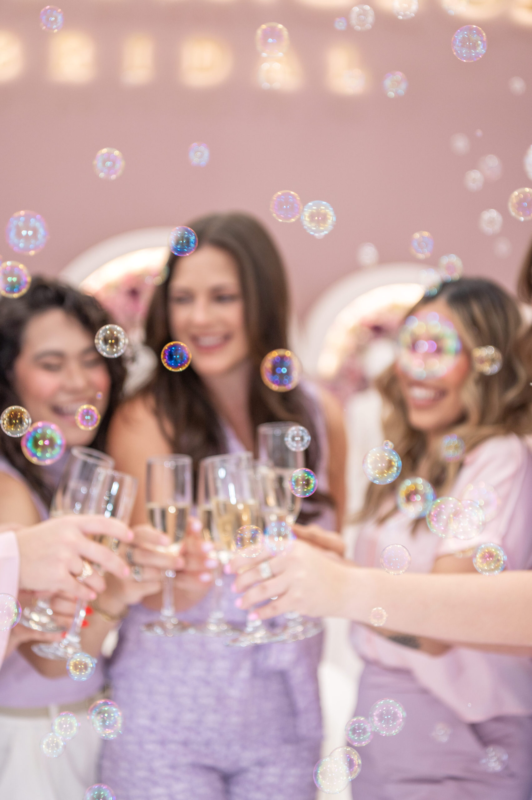 A group of women toasting with champagne glasses in a bridal boutique, surrounded by bubbles floating in the air.