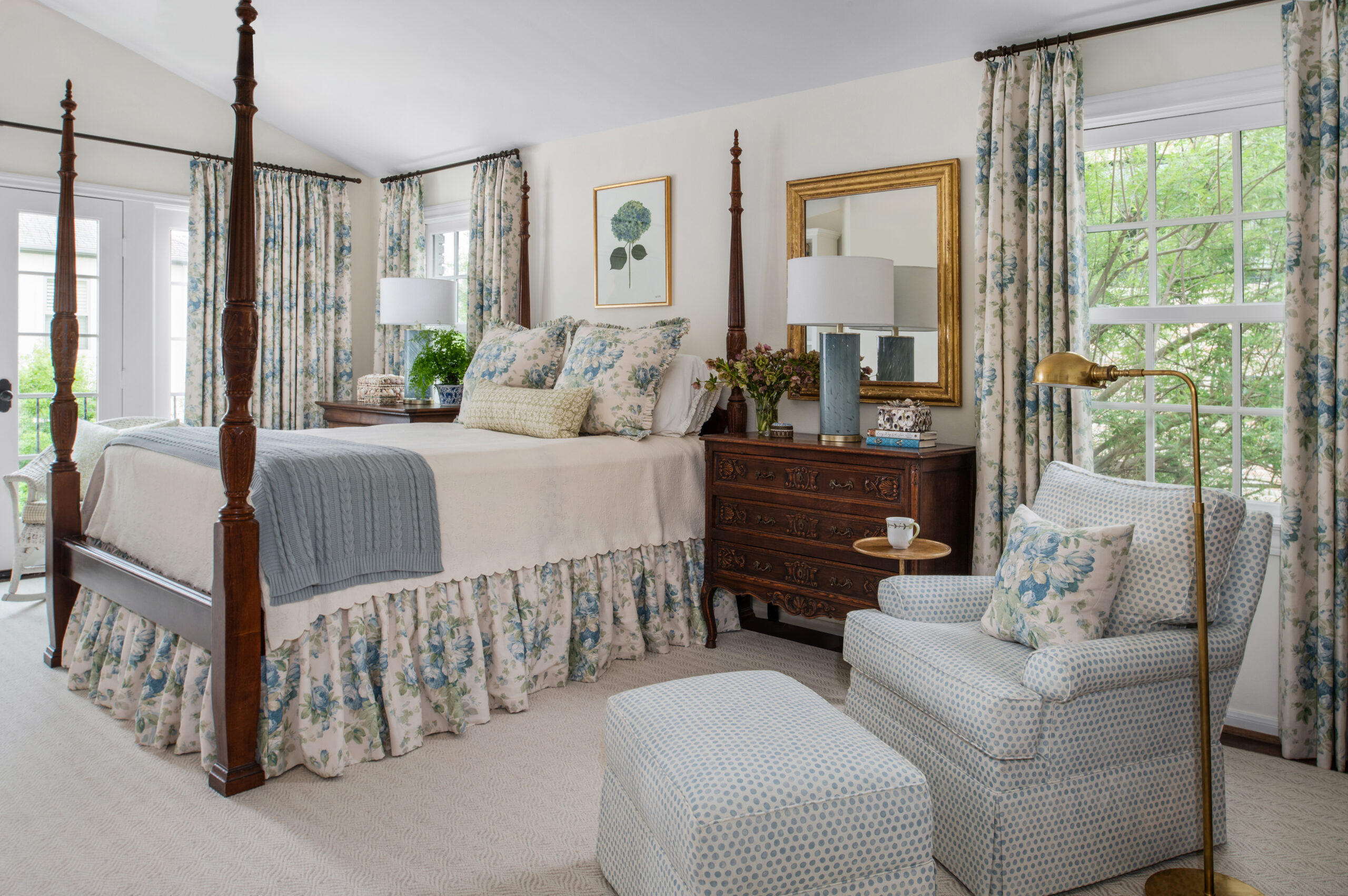 A spacious and elegant master bedroom showcasing a four-poster bed with floral bedding and matching drapes. The classic dark wood furniture contrasts beautifully with the soft blue and floral tones throughout the room. This image exemplifies high-end Interior Design Photography Licensing, capturing the intricate balance between traditional and cozy elements.