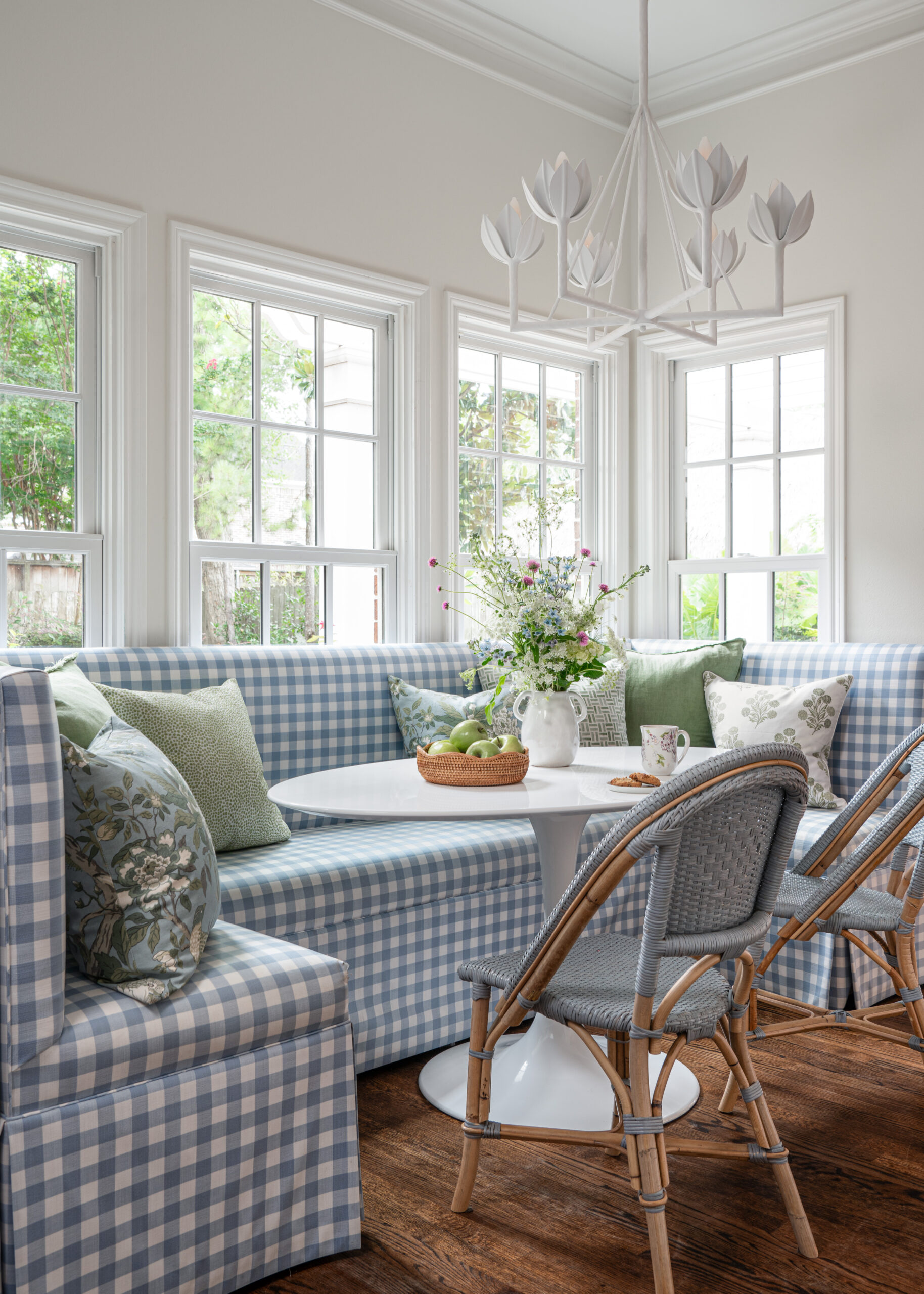 Breakfast nook with a gingham-patterned banquette and bright natural light: This cozy breakfast area features a checkered blue banquette paired with woven chairs and light green throw pillows, creating a fresh and welcoming dining space ideal for Interior Design Photography Licensing.