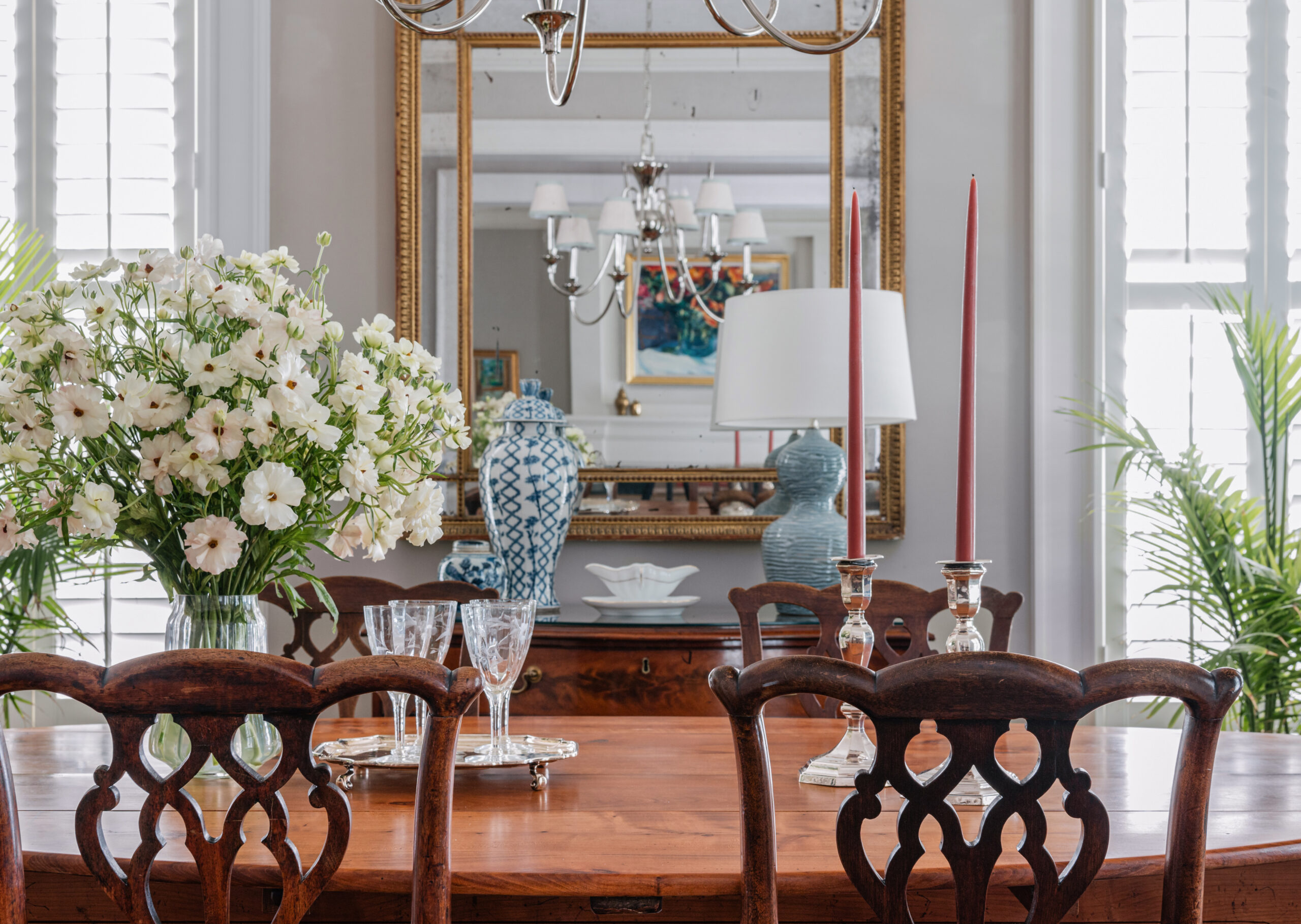 A close-up of the dining room table set with crystal glasses and silver candlesticks. A large mirror behind the table reflects the elegance of the room, with decorative vases and soft lighting enhancing the luxury feel. The detailed craftsmanship and timeless decor make this image perfect for