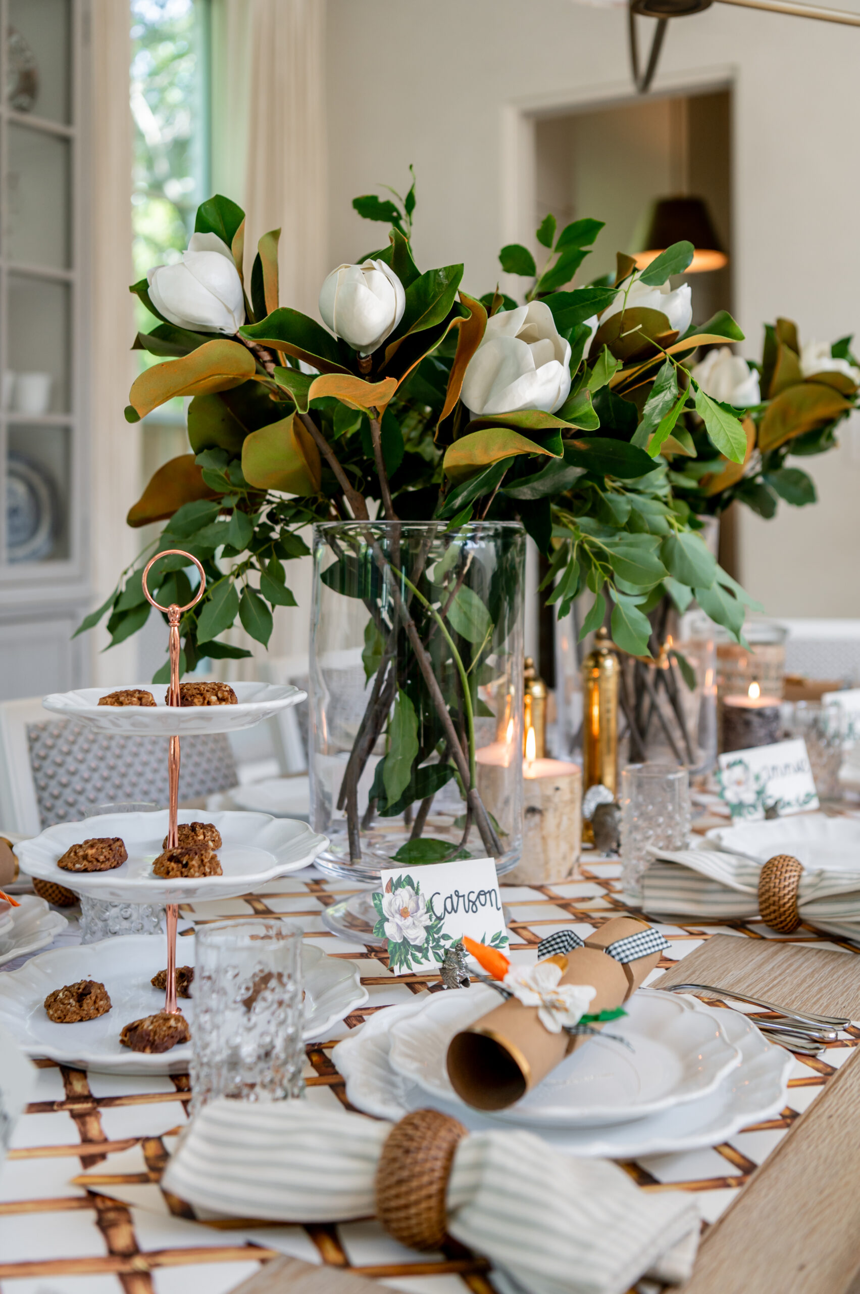 A beautiful close-up of a holiday table setting with magnolia flowers, candles, and seasonal interior design elements like festive place settings and napkin wraps