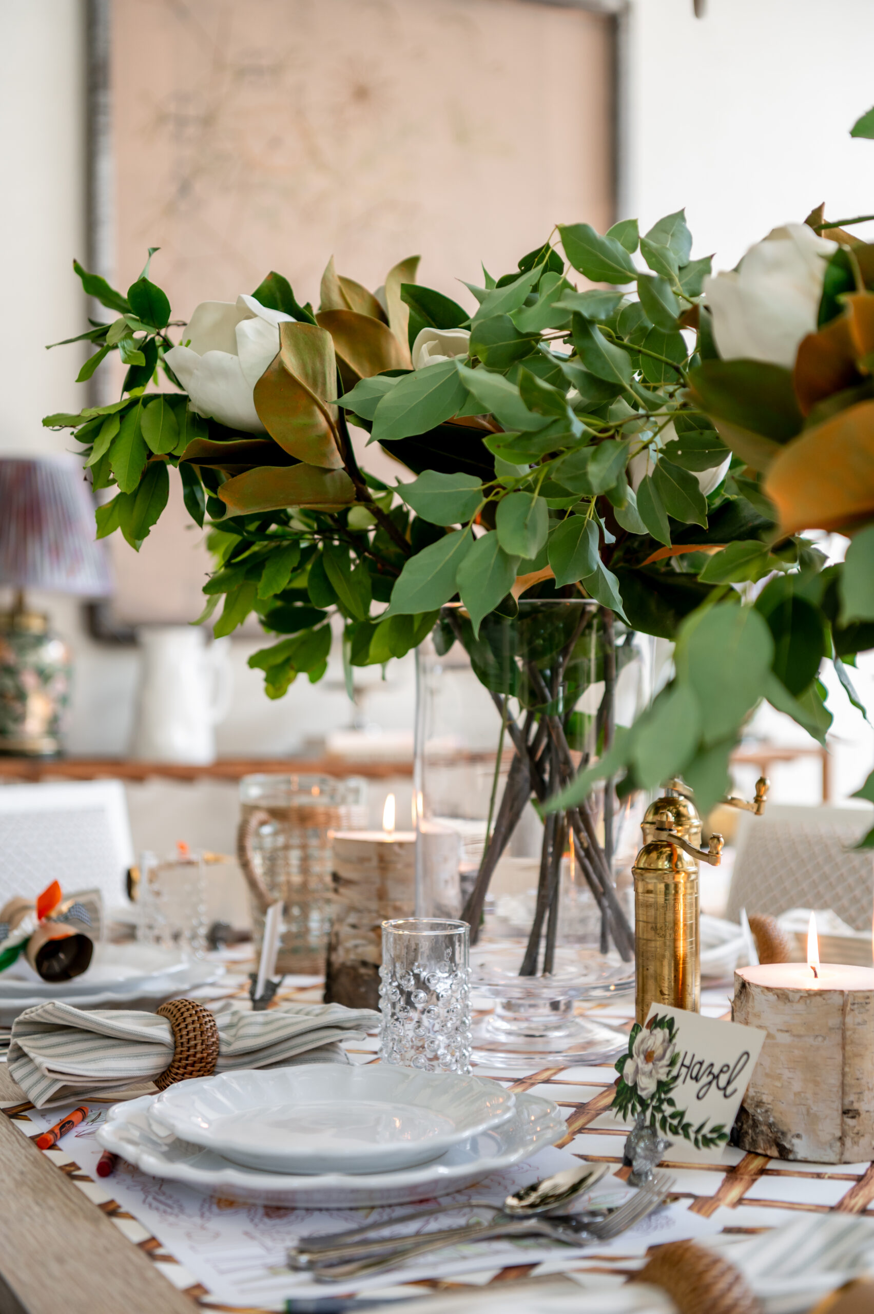 A beautifully styled dining table with seasonal interior design elements, featuring magnolia flower arrangements, candles, and personalized place settings for a holiday gathering