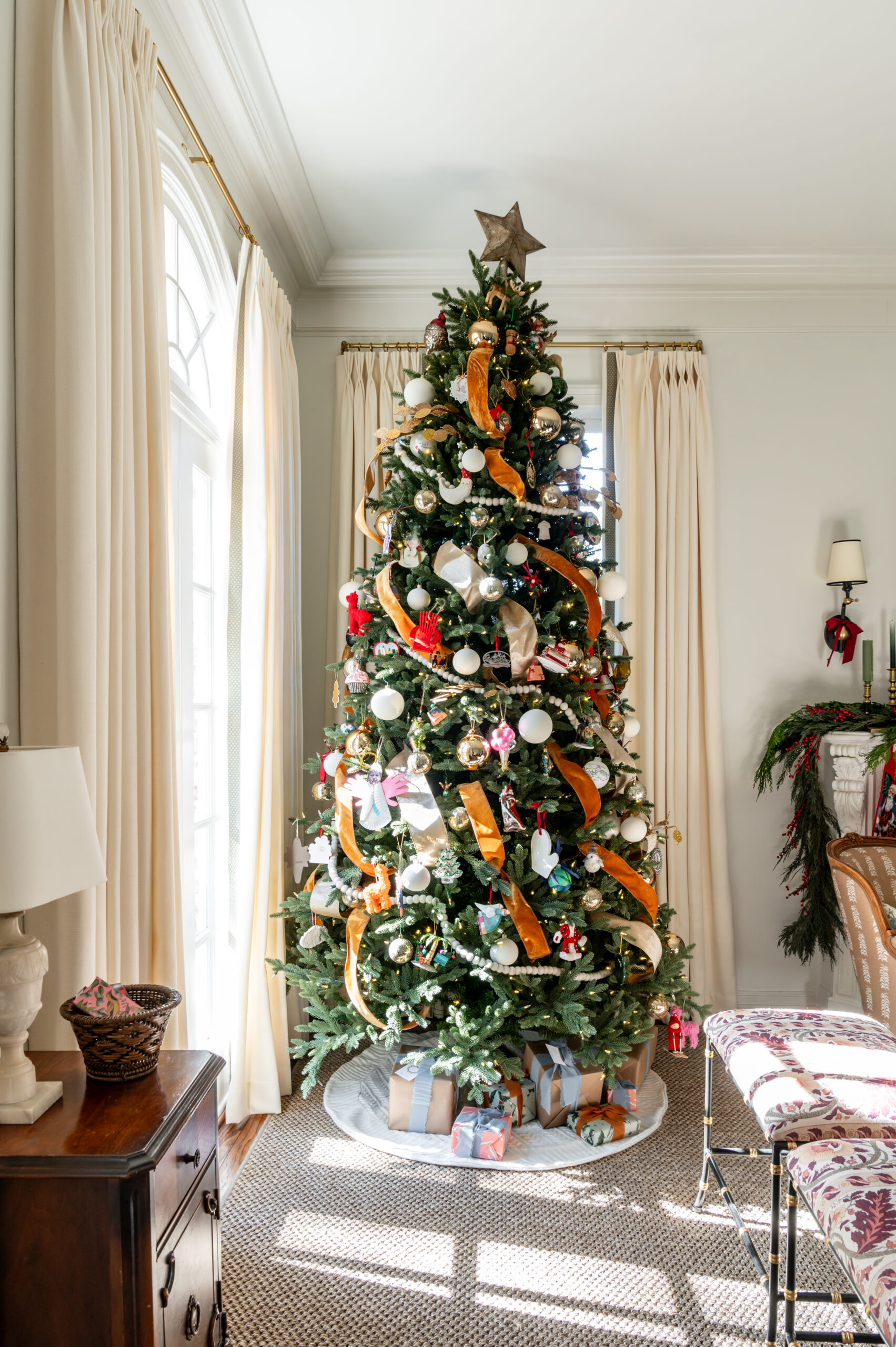 A well-decorated Christmas tree in the background, with a beautifully styled living room featuring seasonal interior design elements, such as gifts and festive décor.