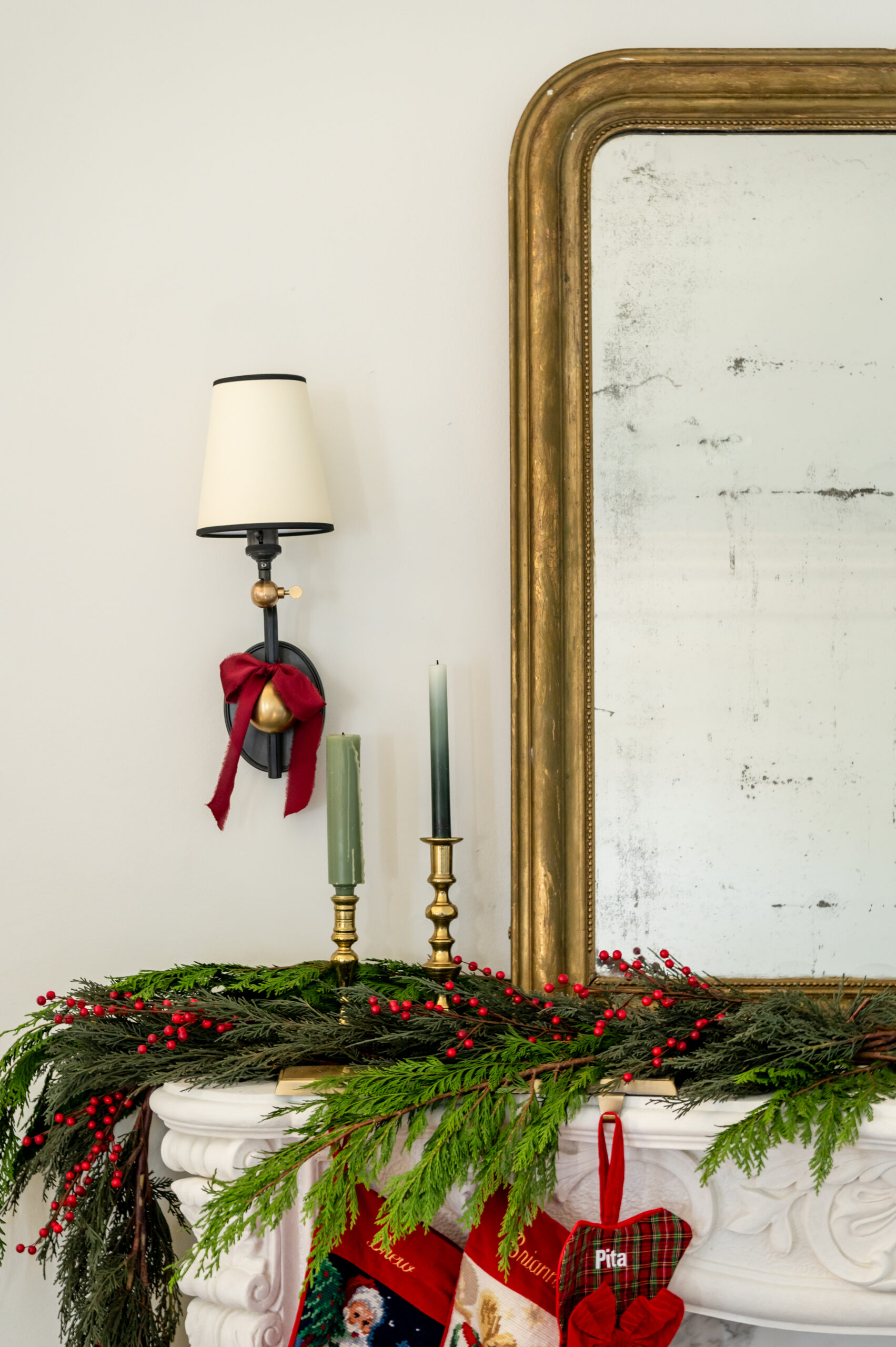 A close-up of a fireplace mantel adorned with seasonal interior design elements, including festive red ribbons, green candles, and seasonal greenery, creating a cozy holiday atmosphere.