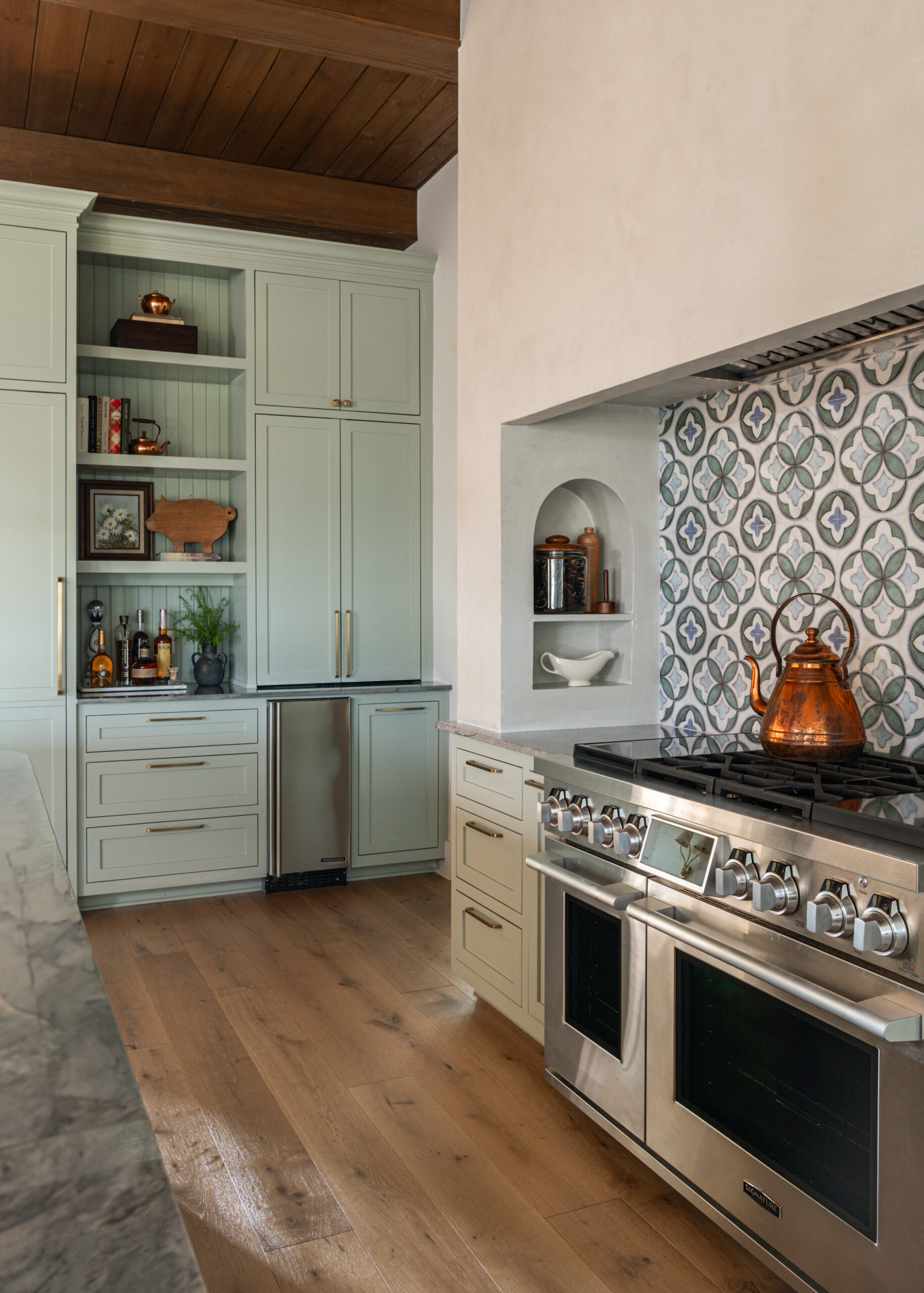 Beautiful custom interior design kitchen with sage green cabinetry, a unique tile backsplash, and stainless steel appliances.