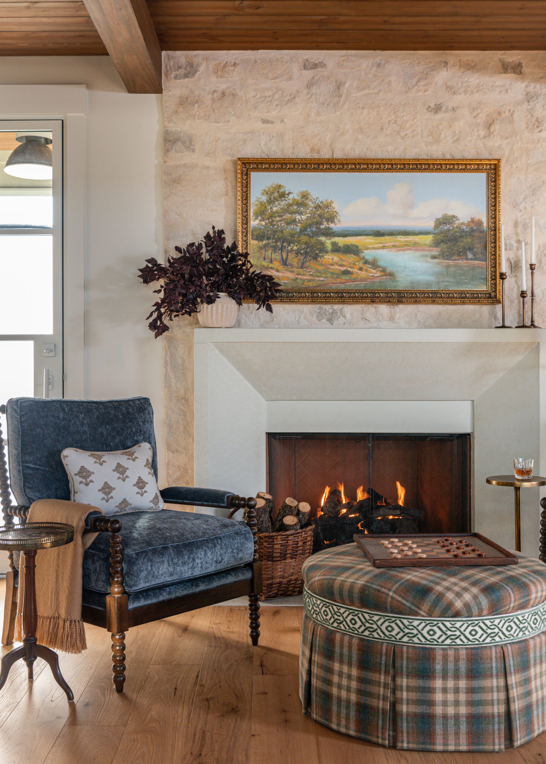 Cozy fireplace nook with custom interior design touches, featuring a vintage painting above the mantle and a comfortable chair.