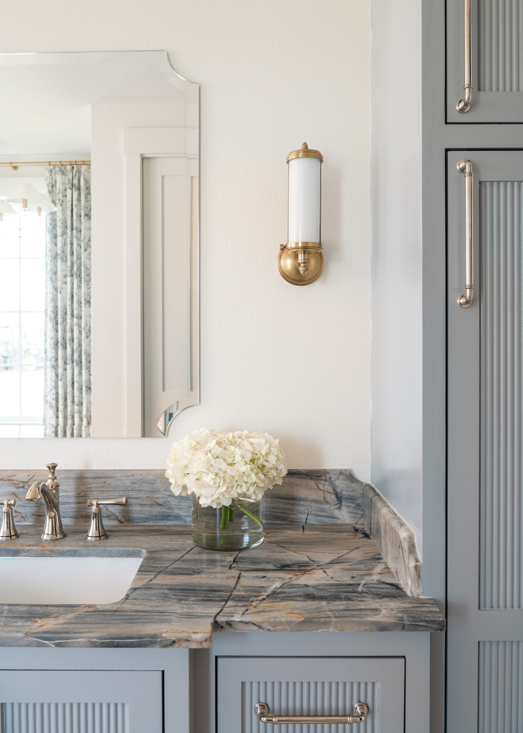 Elegant bathroom vanity area featuring custom interior design with marble countertops, chic light fixtures, and beautiful flowers.