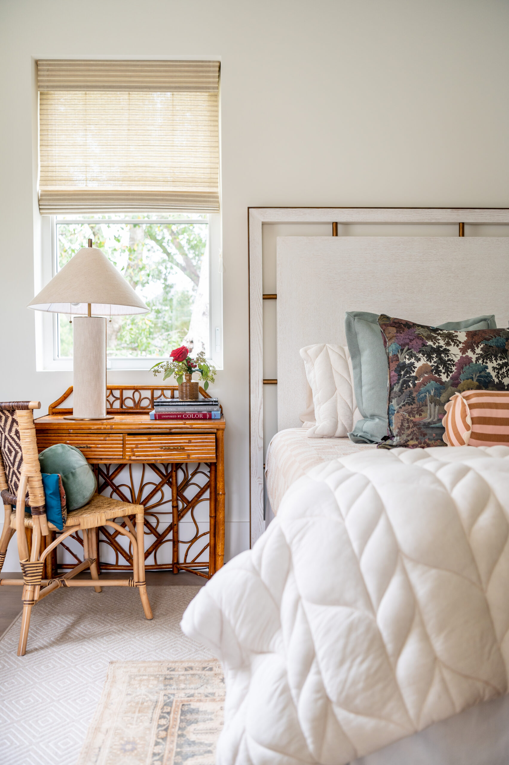 A serene bedroom with a rattan desk, soft bedding, and a mix of patterned pillows, demonstrating a master interior design style that blends natural elements with comfort and elegance.