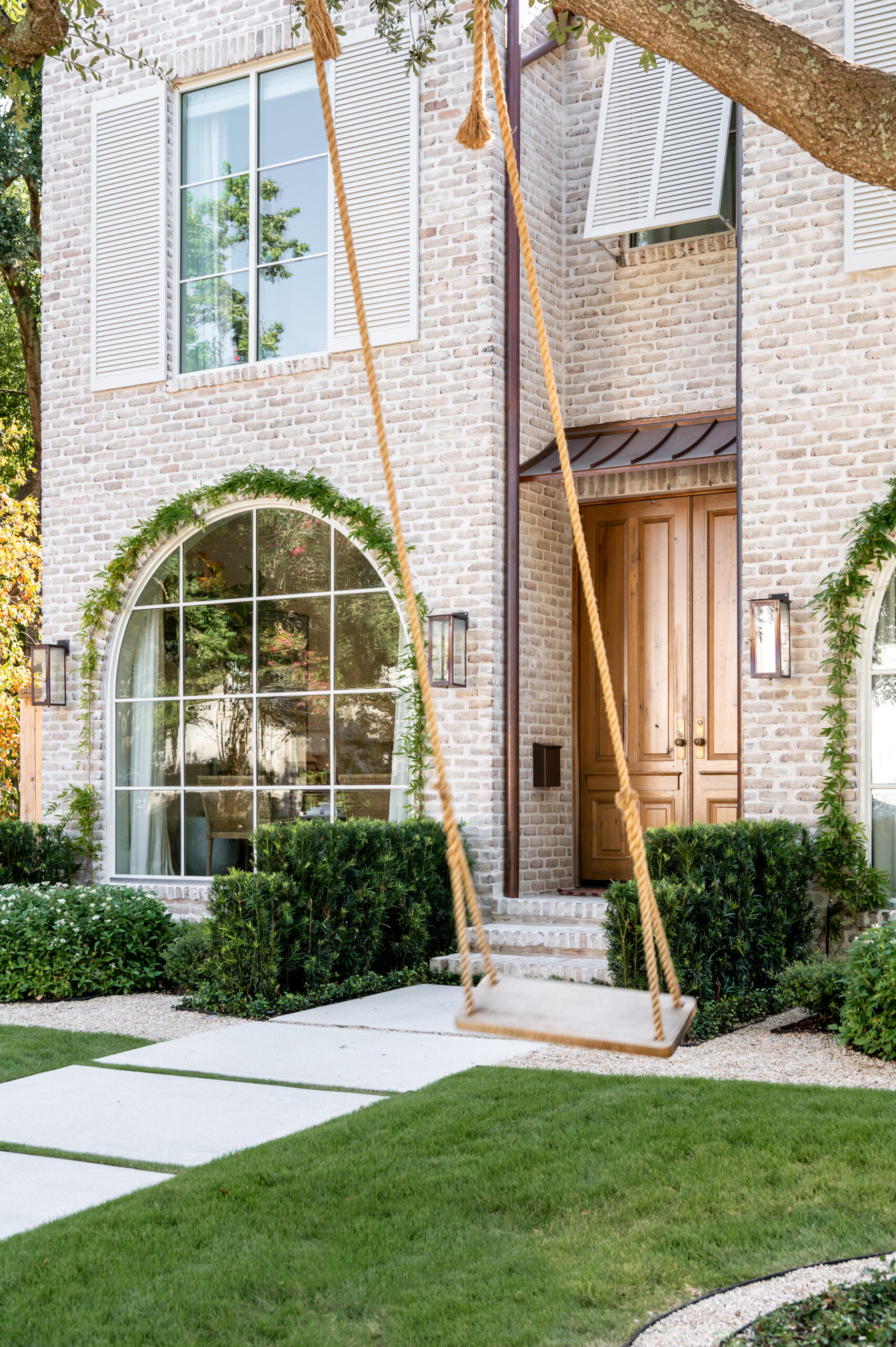 The front exterior of a house with a charming swing under a lush tree, showcasing a well-curated landscape design that complements the master interior design of the home."