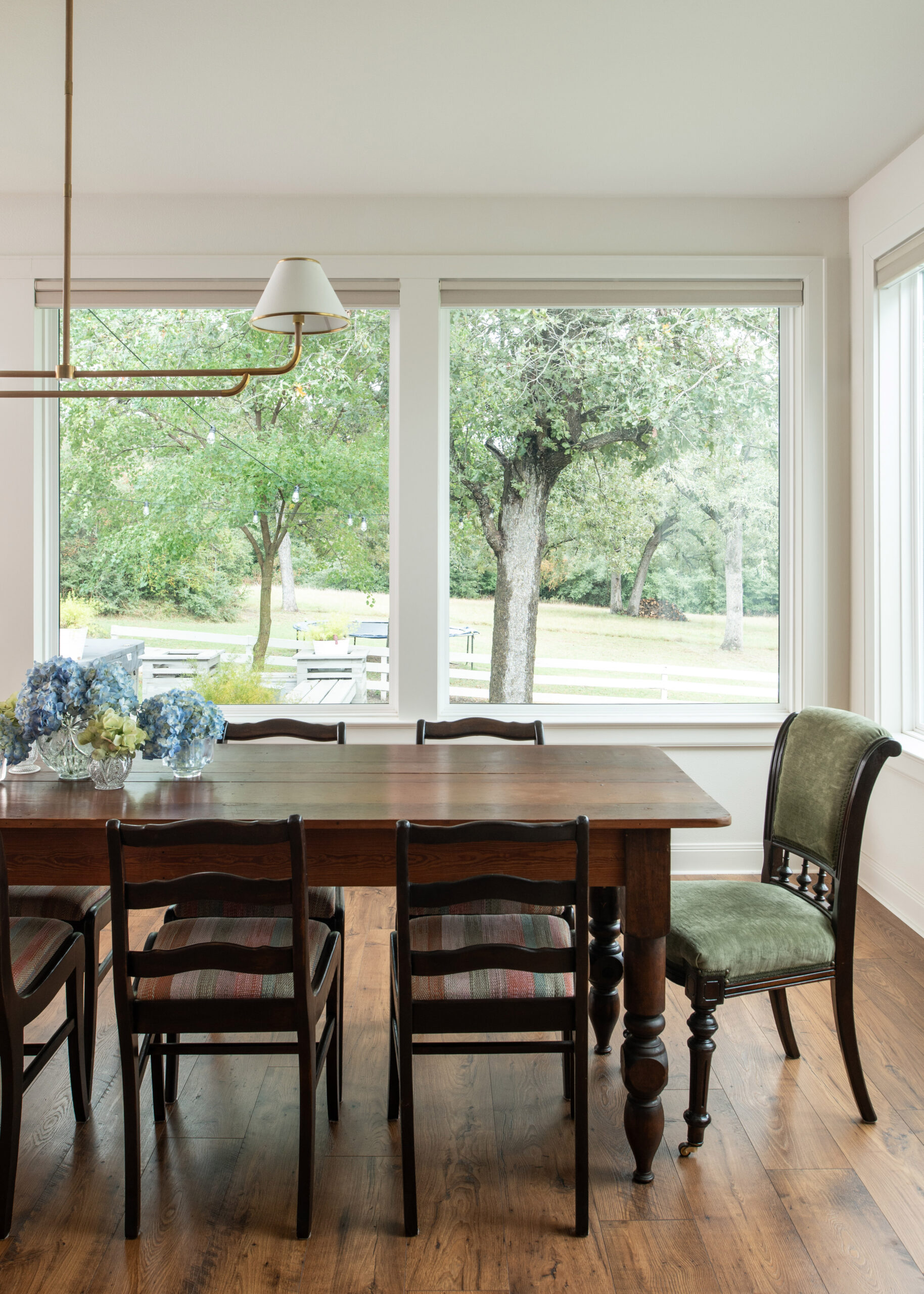 Elegant dining room with large windows letting in plenty of natural light, showcasing a wood dining table with colorful floral arrangements. The blend of natural elements and contemporary furniture exudes timeless modern interior design.