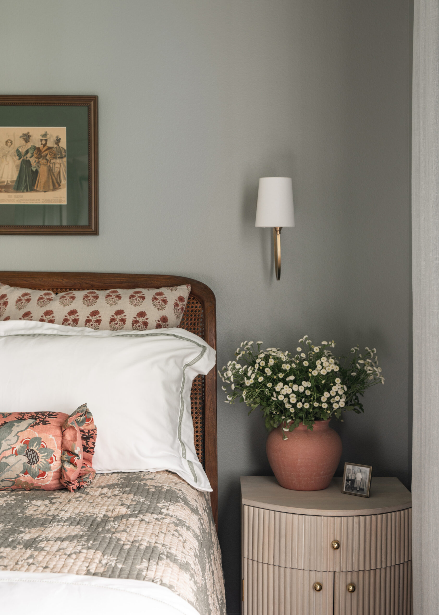 Close-up of a bedroom corner with a warm-toned nightstand, a beautiful potted plant, and a cozy bed setup. The room feels airy, with a timeless modern interior design influence.