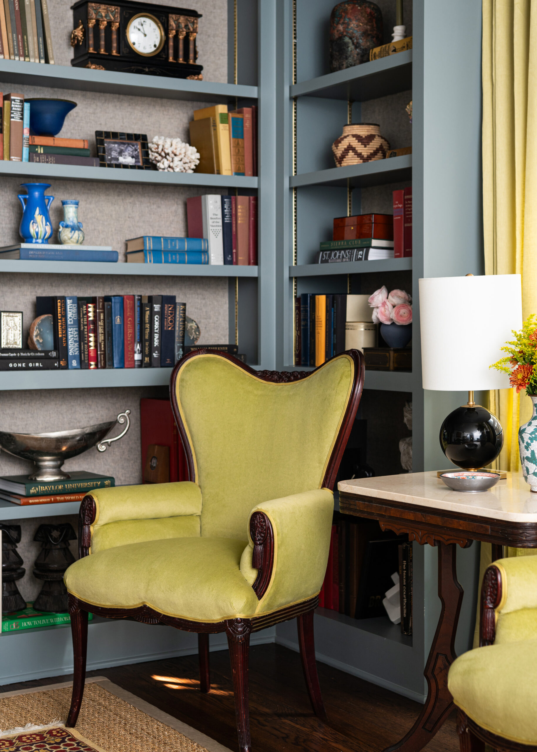 A close-up shot of a vintage green chair with a beautiful, eclectic bookshelf background. The interior design and photography perfectly highlight the color contrast.