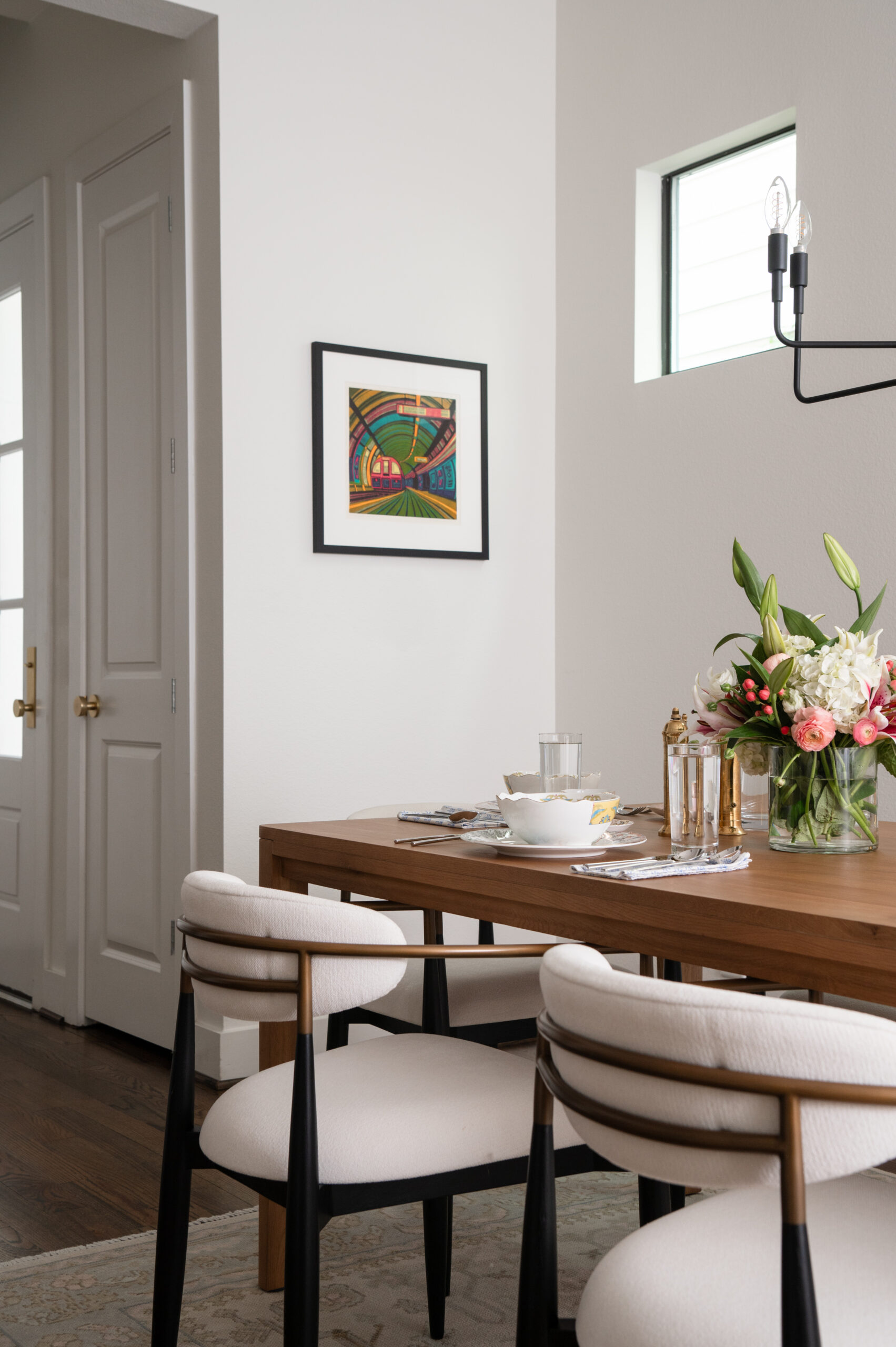 A bright and modern dining room with contemporary artwork on the walls, a floral centerpiece, and sleek white chairs. This space is thoughtfully designed as part of a master interior design plan that balances aesthetics with comfort.