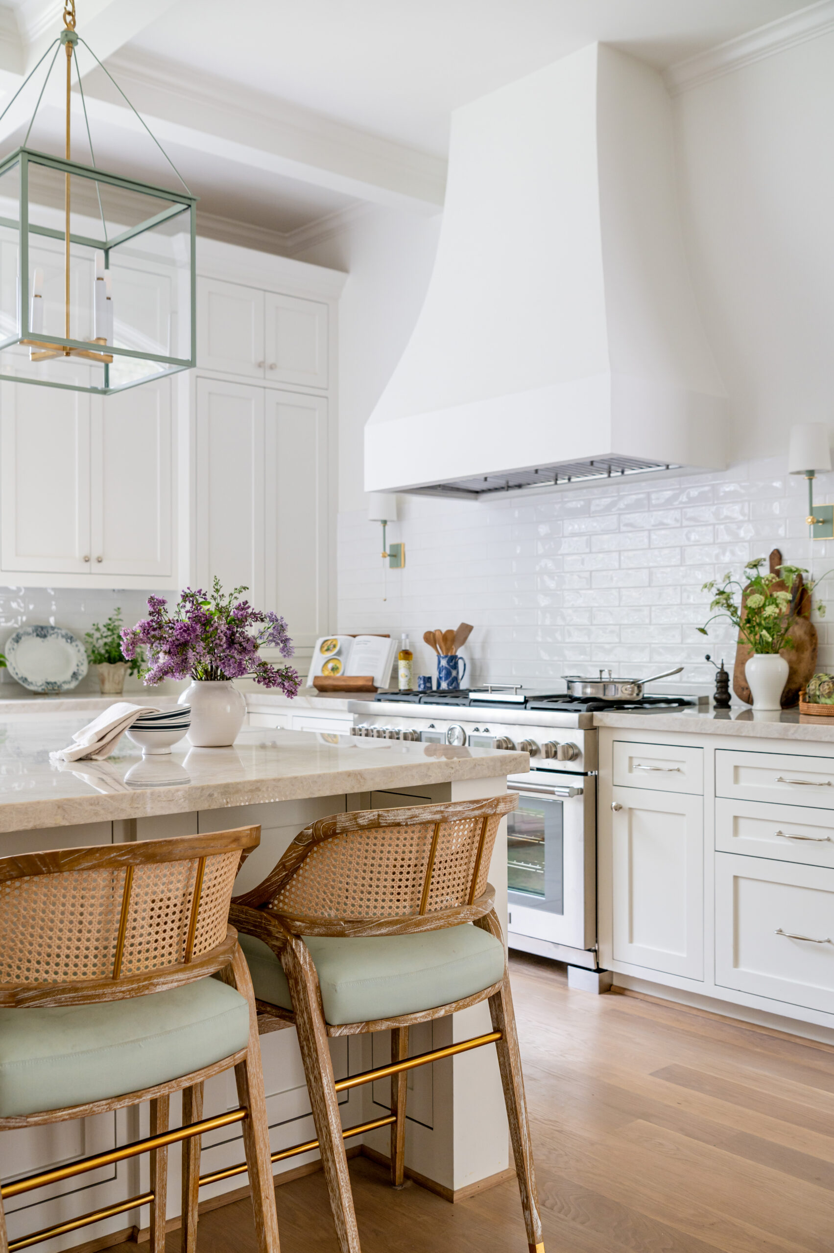 An elegant kitchen with white cabinetry, marble countertops, and stylish rattan bar stools, ideal for featuring in luxury interior design publications.