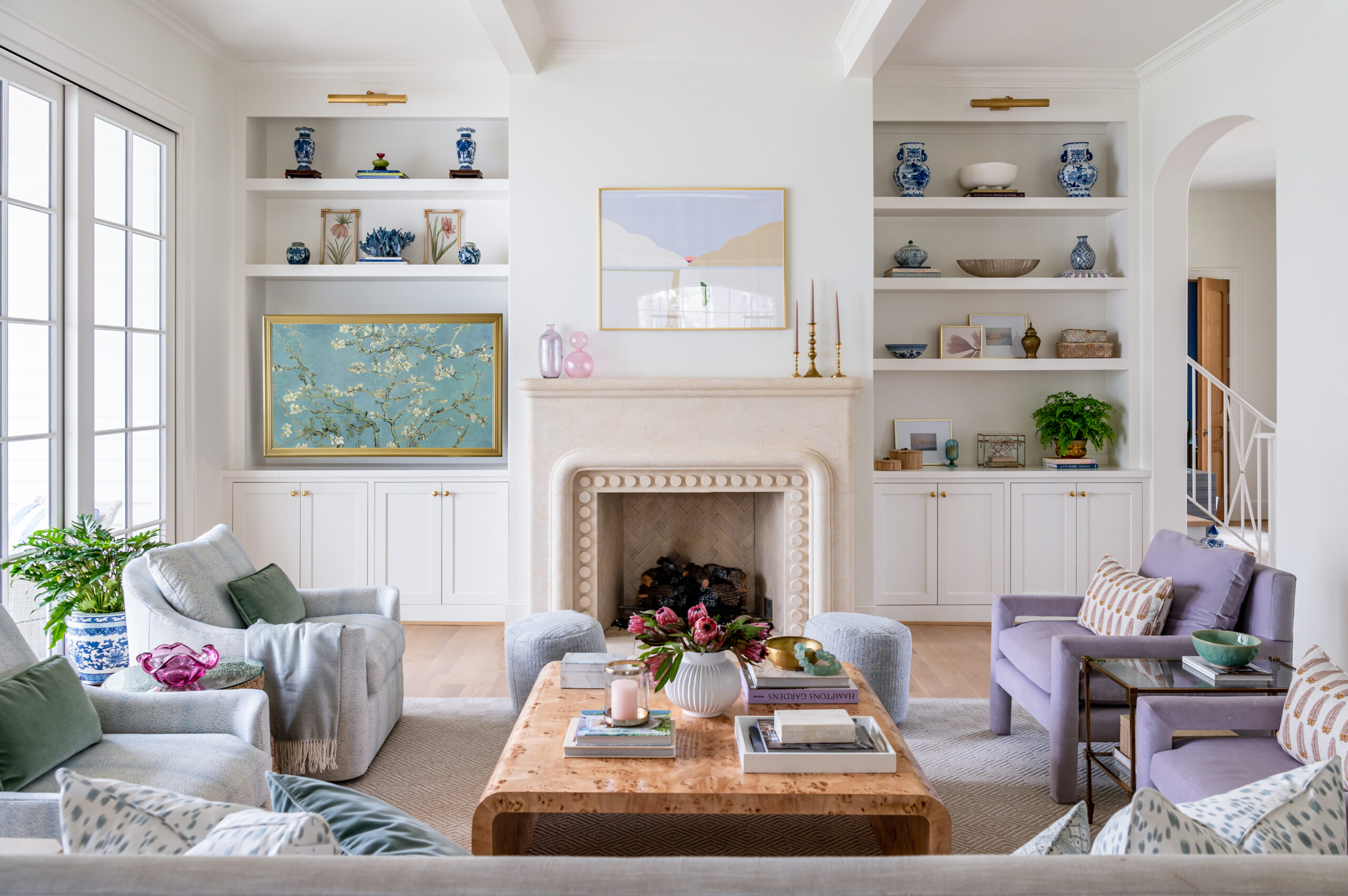 A light and airy living room with soft blue and purple accents, framed art, and curated shelves with personal decor, seen in top-tier interior design publications.