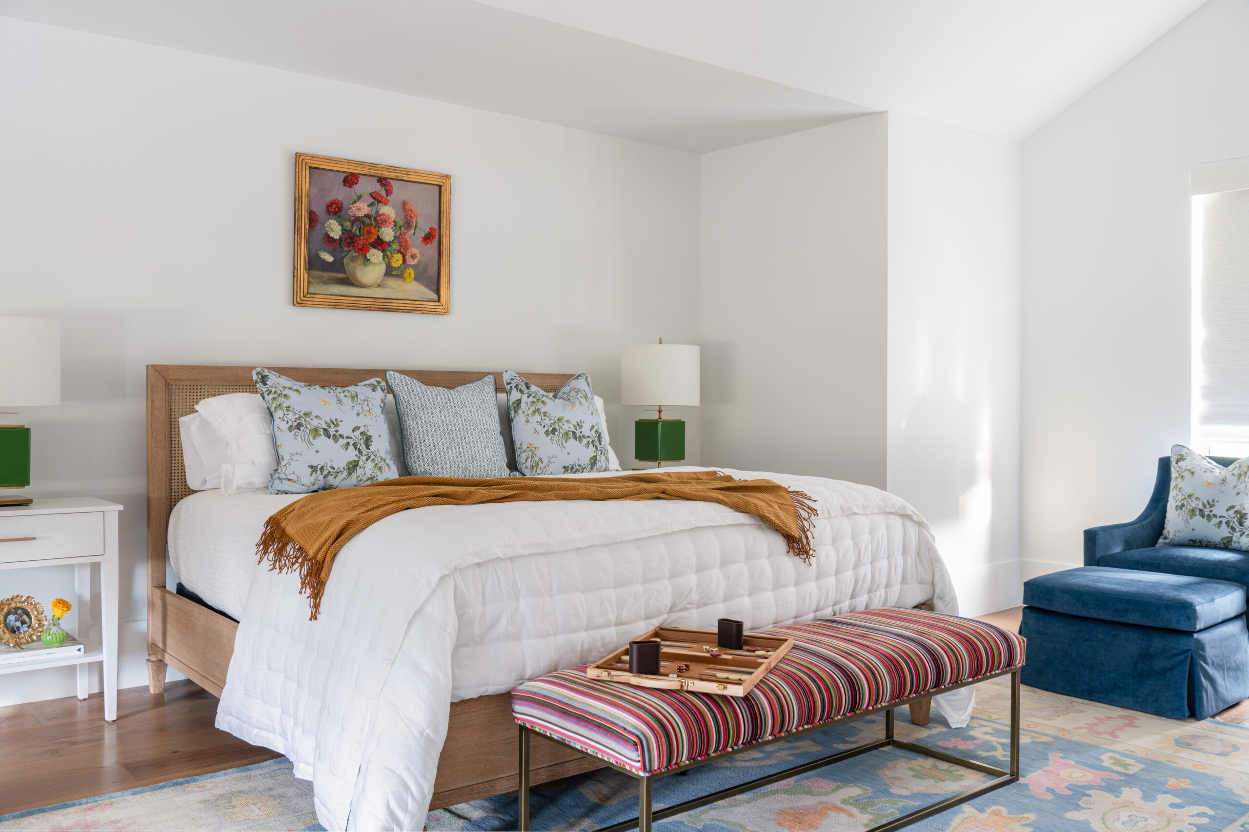 A cozy bedroom with a striped bench, warm blankets, and a colorful painting above the bed.