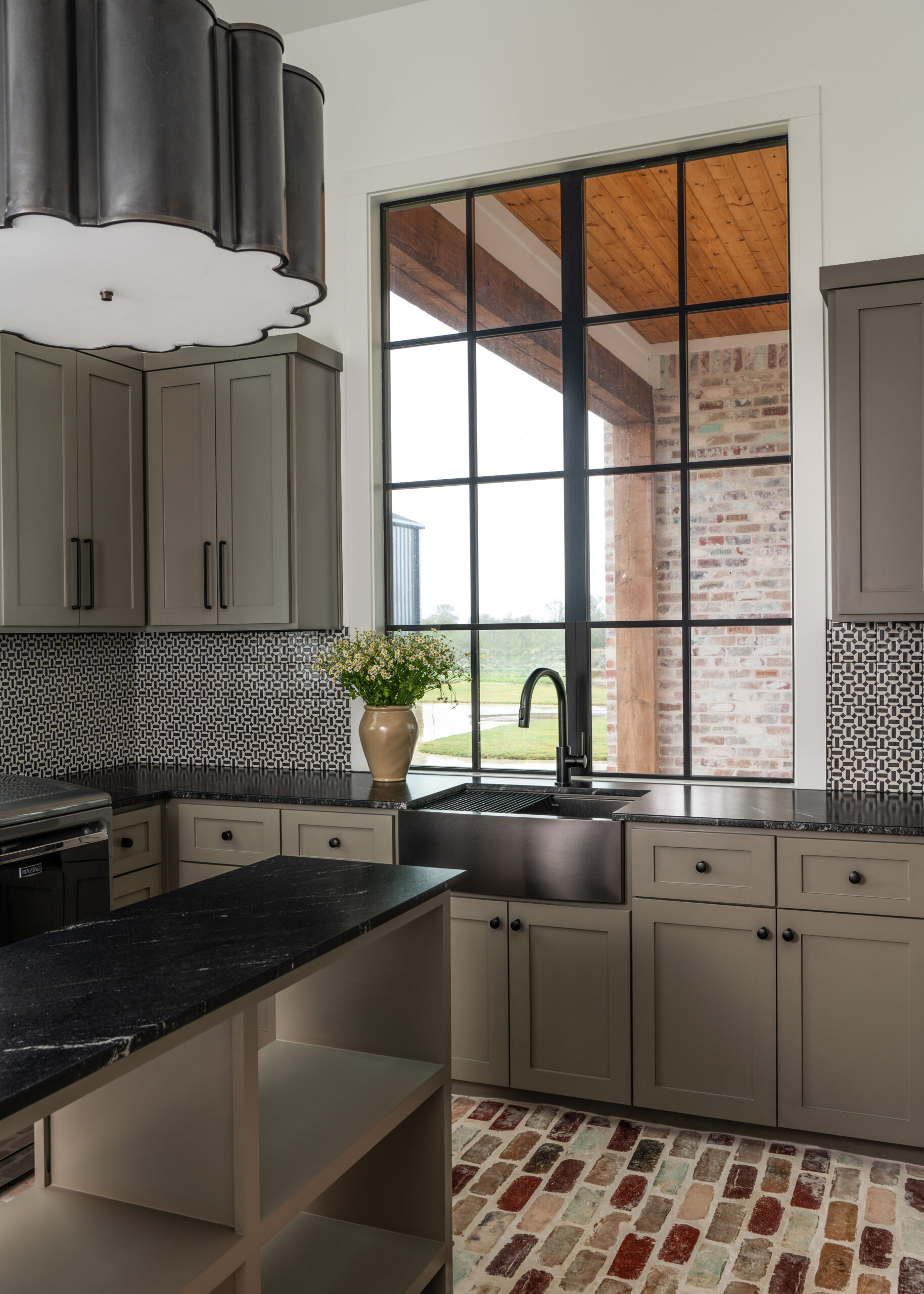 Stylish modern kitchen with dark cabinetry, stainless steel sink, and large windows offering a stunning view of the outdoor greenery, perfect for a cozy home.