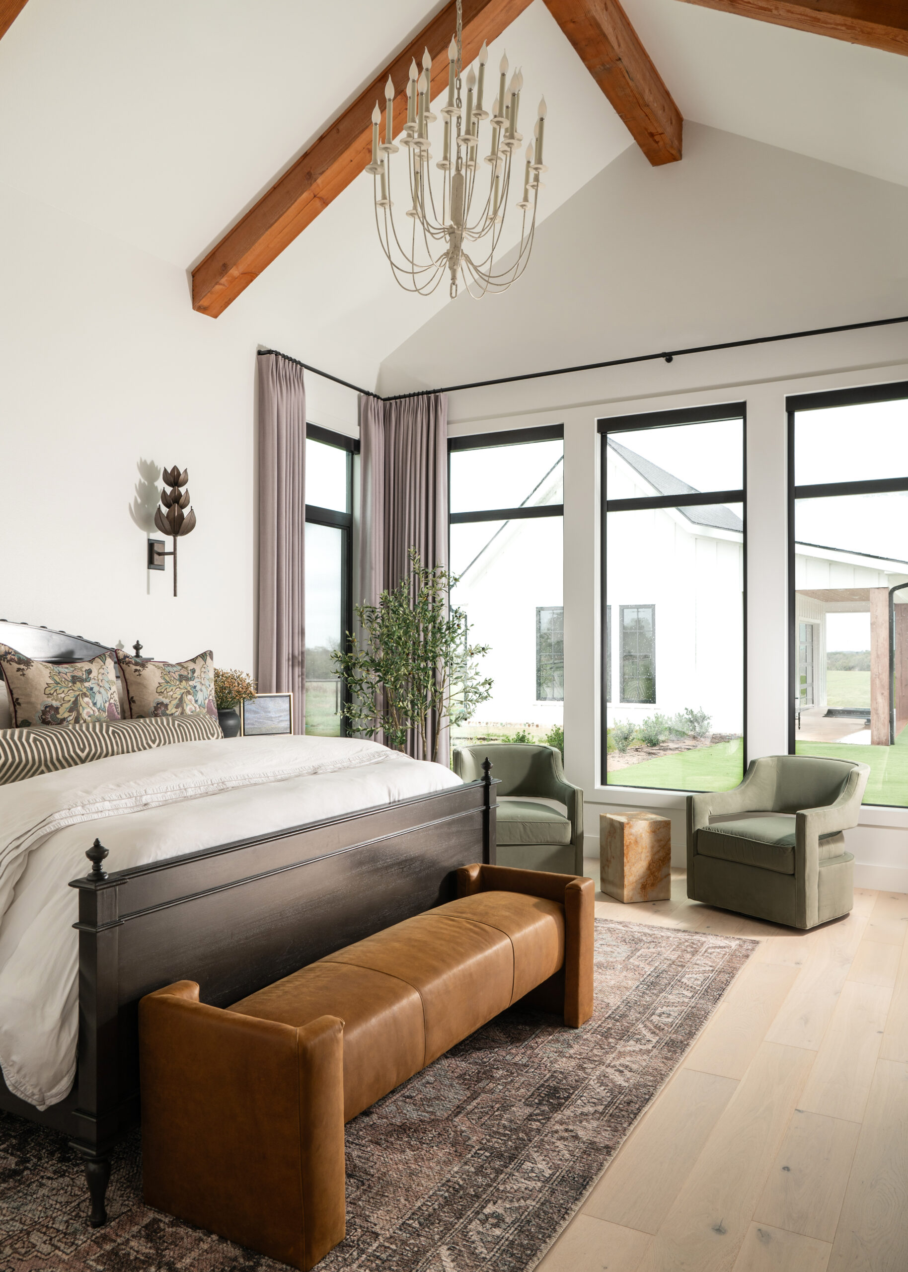 Modern bedroom with a statement leather bench, tall windows offering natural light, and a blend of neutral tones and contemporary accents.