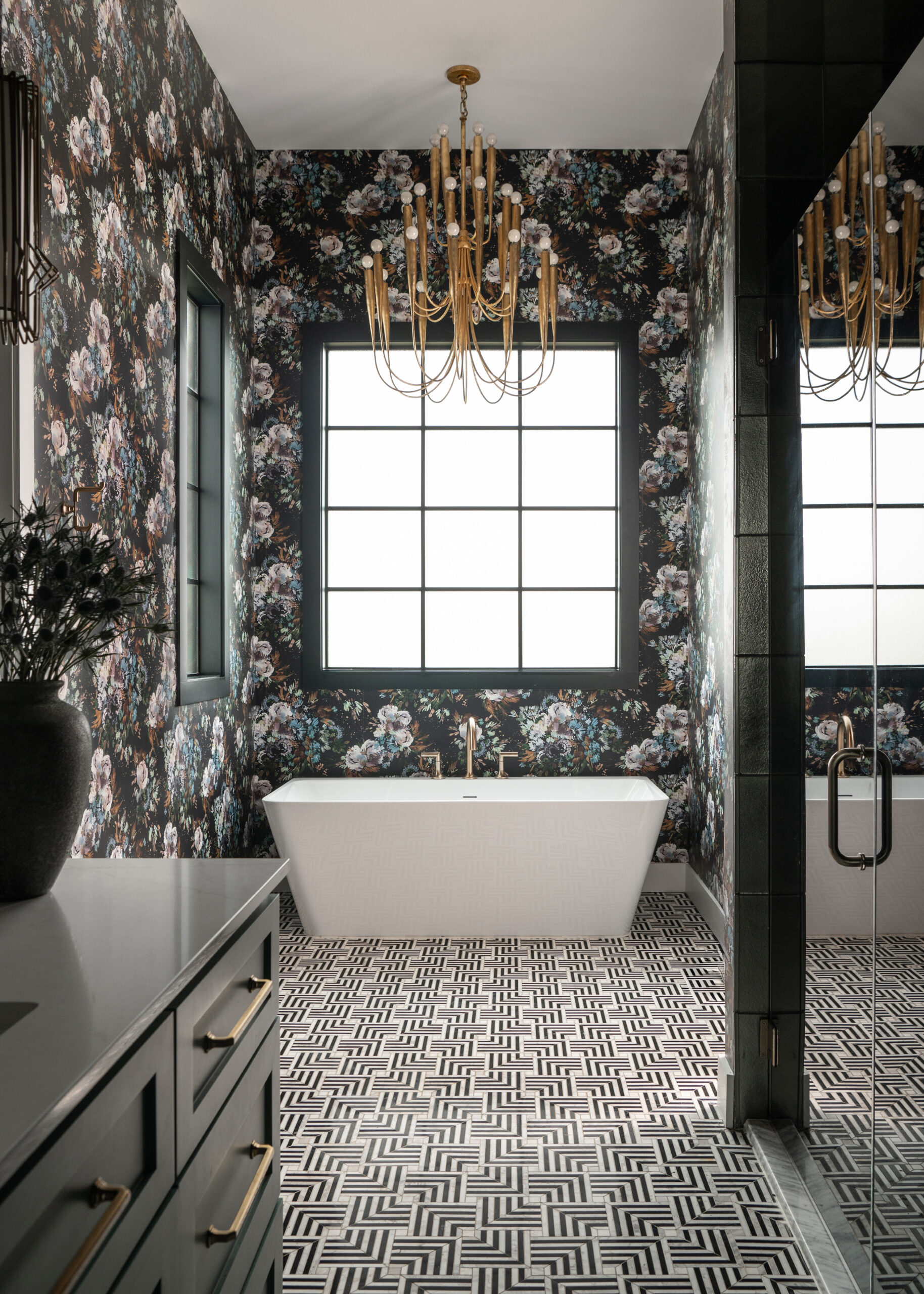 Contemporary bathroom with a freestanding white bathtub, dark floral wallpaper, and elegant golden lighting fixtures, creating a beautiful spa-like ambiance