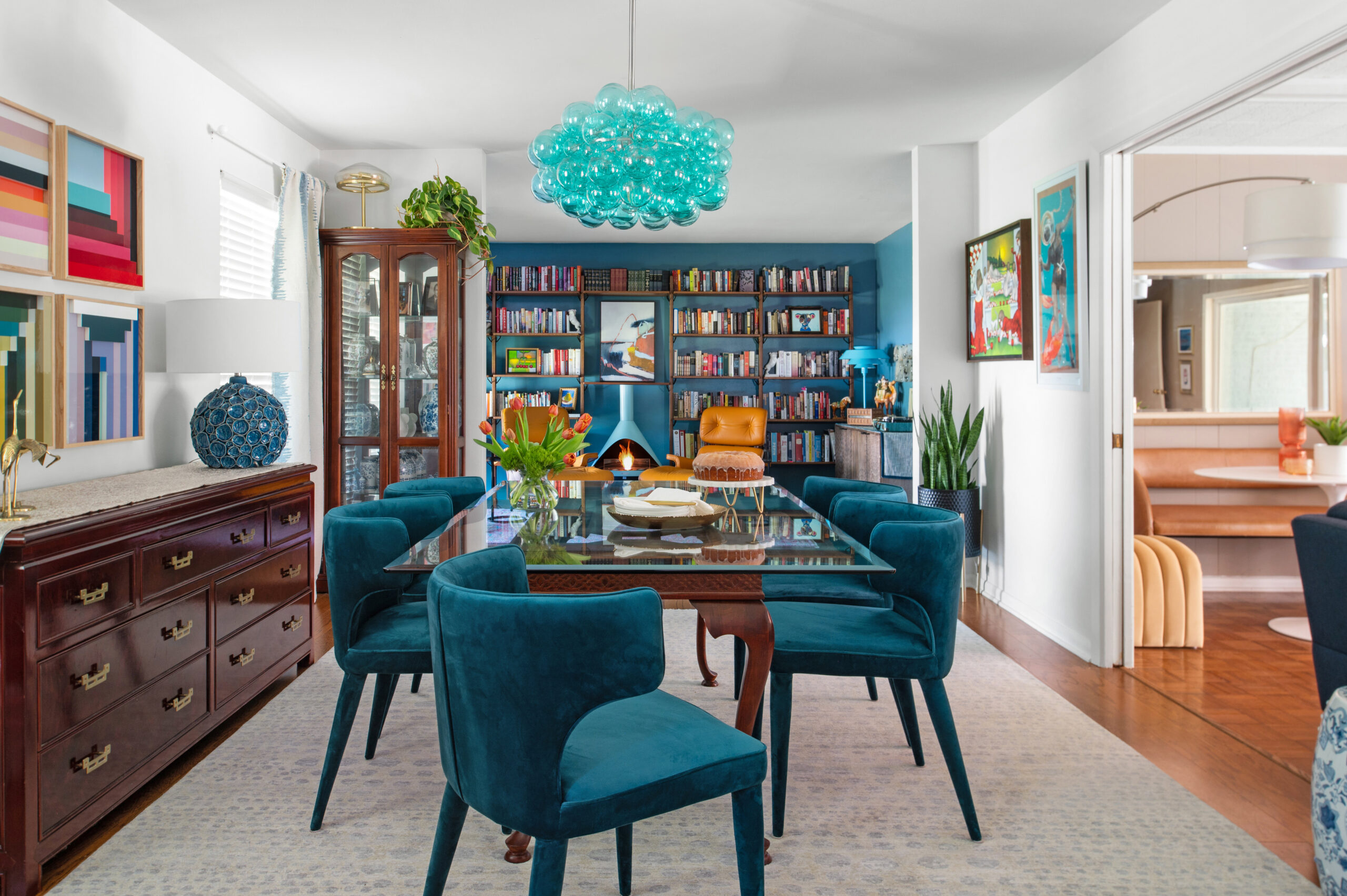 A colorful dining room with a blue chandelier, art-filled walls, and luxurious velvet chairs, perfect for a feature on bold home designs in interior design publications.