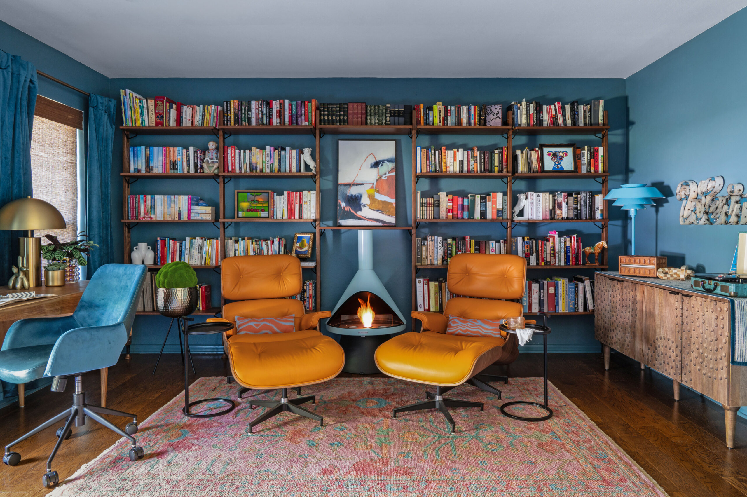 A stylish reading corner with vintage armchairs and colorful modern art against dark blue walls. Perfect for interior design publications focusing on bold, personal home spaces.

